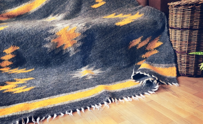 May include: A gray and yellow woven throw blanket with a fringed edge. The blanket is folded and draped over a wooden surface.