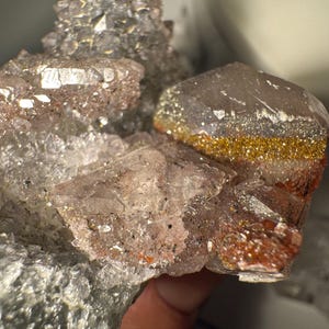 May include: Close-up of a cluster of quartz crystals. The crystals have a clear, translucent appearance with areas of gold and reddish-brown coloration. The crystals are clustered together, creating a textured and sparkling effect.