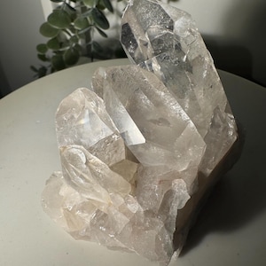 Pode incluir: Um grande grupo de cristais de quartzo transparente com múltiplas terminações pontiagudas e translúcidas que surgem de uma base sólida. O espécime mineral apresenta facetas naturais, bordas afiadas e inclusões internas com uma superfície brilhante.