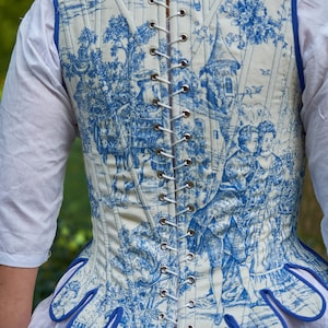 May include: A white and blue patterned corset with a blue trim and a lace-up back. The corset has a scalloped bottom edge.
