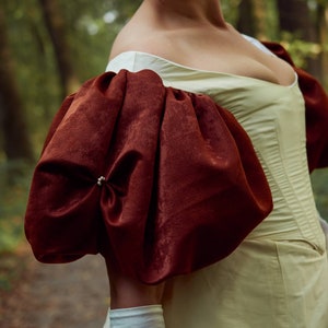 May include: A close-up of a woman's off-the-shoulder dress with a fitted bodice and large, puffy sleeves. The sleeves are a deep burgundy color and the bodice is a pale yellow.