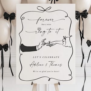 Puede incluir: Un letrero de boda sobre un caballete con el texto "forever has a nice ring to it". El letrero está rodeado de globos blancos con lazos negros. El letrero también dice "Let's Celebrate Adelene & Thomas".