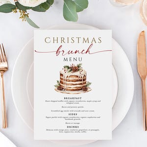 May include: A white menu card with the words "Christmas Brunch Menu" in gold and burgundy script. The menu features a watercolor illustration of a layered cake with pine cones. Gold forks, knives, and spoons are arranged around the plate.