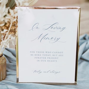May include: A white framed sign with a gold border, featuring the text "In Loving Memory" in blue cursive script. The sign also includes the text "For those who cannot be here today, but are forever present in our hearts. Today and always." in smaller blue text.