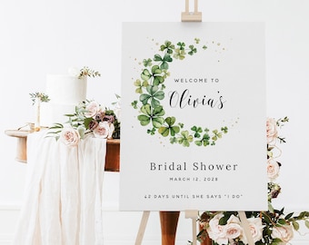 Könnte beinhalten: Ein weißes Schild mit einem Kranz aus grünen Kleeblättern und goldenem Glitzer. Auf dem Schild steht "Willkommen zum Bridal Shower von Olivia am 12. März 2028 42 Tage bis sie 'Ja' sagt"