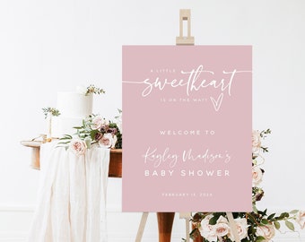 May include: A pink welcome sign with white text announcing a baby shower for Kayley Madison. The sign reads "A little sweetheart is on the way!" and "Welcome to Kayley Madison's Baby Shower" with the date "February 15, 202X".