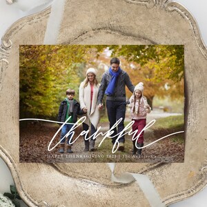 Puede incluir: Una familia de cuatro personas camina por un sendero en un bosque oto&ntilde;al. Los padres van de la mano con sus dos hijos. El texto "thankful" est&aacute; escrito en cursiva blanca en la parte inferior de la imagen. El texto "Happy Thanksgiving 2021 | The Anderson's" est&aacute; escrito en blanco debajo del texto en cursiva.