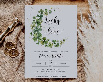 Könnte beinhalten: Eine hellblaue Einladung zu einer Brautparty mit einer Aquarell-Illustration eines Kleeblatt-Kranzes. Der Text "Lucky in love" ist in Kursivschrift geschrieben. Die Einladung ist für Olivia Wildes Brautparty am 12. März 2025 um 10:00 Uhr im Villa & Vine Chateau in Santa Barbara.