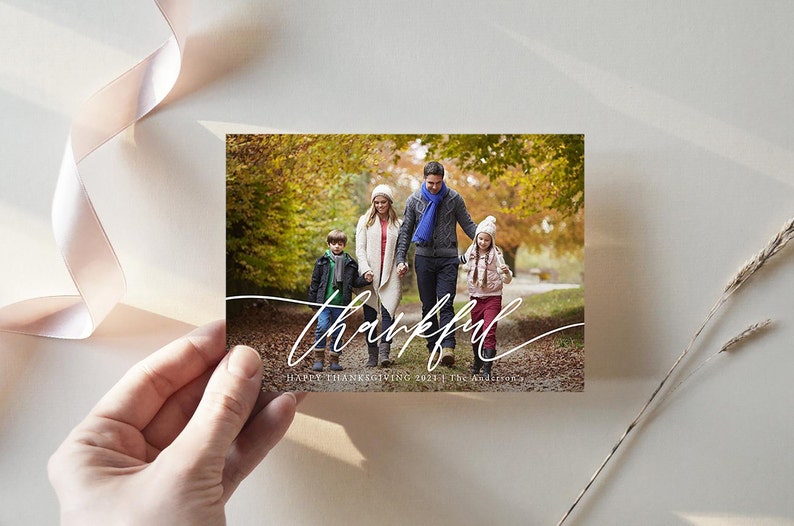 Puede incluir: Una tarjeta de Acci&oacute;n de Gracias con una familia de cuatro personas caminando por un bosque de oto&ntilde;o. La tarjeta tiene la palabra "thankful" escrita en cursiva blanca y el texto "Happy Thanksgiving 2021 | The Anderson's".