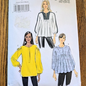 May include: Vogue Patterns sewing pattern V9059. The pattern features illustrations of three different blouses. The top left of the pattern reads "V9059" and "VOGUE PATTERNS". The pattern is on a wooden surface.