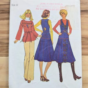 May include: A vintage Simplicity sewing pattern envelope, size 12, featuring illustrations of three women in 1970s-style outfits. The envelope is white with green text and the text "Simplicity". The outfits include a red top, blue dresses, and tan pants.