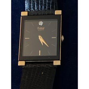 May include: A rectangular black Pulsar Quartz watch with gold accents and a black leather band. The watch face is black with gold hands and a small diamond at the 12 o'clock position. The watch band is black.