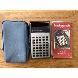 May include: A vintage Texas Instruments TI-30 calculator with a blue case and owner's manual. The calculator has a black and silver design with numerous buttons and a display screen. The manual is red and white.