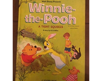 Puede incluir: Un libro infantil vintage de "Winnie-the-Pooh" con una cubierta amarilla. El título está en letras grandes rojas y blancas. Las ilustraciones incluyen a Winnie the Pooh, Rabbit y Christopher Robin. El libro se titula "A Tight Squeeze" de A.A. Milne.