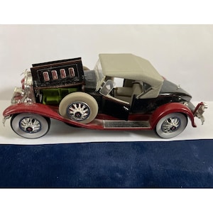 May include: A detailed model of a classic convertible car. The car features a black body with red fenders, a tan convertible top, and white-walled tires. The wheels have a silver hubcap design. The car's interior is visible with open doors.