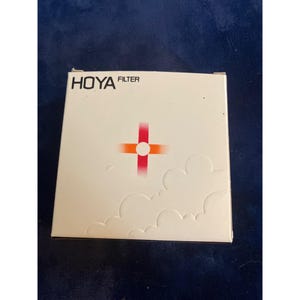 May include: A white box with the text "HOYA FILTER" in black. The box features a red and orange cross design with a white circle in the center. The bottom of the box has a cloud-like design.