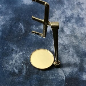 May include: A metallic display stand featuring a circular base and a vertical support arm with three horizontal prongs extending outward. The structure is finished in a polished gold tone, providing a stable platform for holding small items upright.