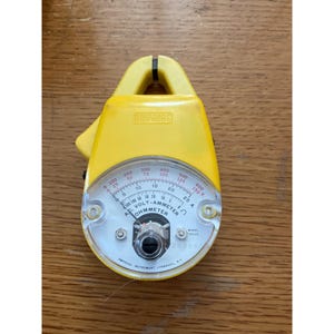 May include: A yellow Amprobe AC volt-ammeter ohmmeter with a clamp top. The device features a clear circular analog display with black and red numerical scales, a central adjustment knob, and the text Amprobe Instrument Lynbrook, N.Y. printed.