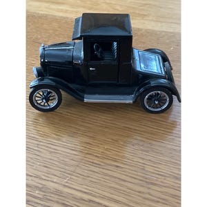 May include: A black vintage toy truck with a detailed design. The toy truck has a cab, a bed, and four wheels. The wheels have a spoke design. The truck is made of a shiny material and sits on a wooden surface.