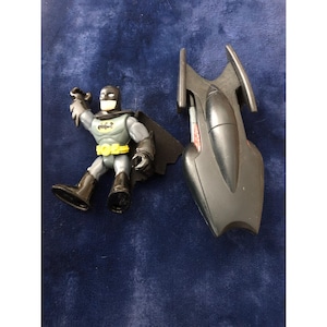 May include: A black and gray plastic Batman action figure with a yellow utility belt and a black cape. The figure is holding a black batarang in its right hand. The figure is standing next to a black plastic Batmobile.