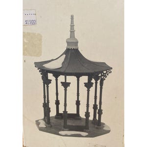 May include: A detailed, grayscale image of a miniature gazebo. The gazebo features a dark, ornate roof and supporting pillars. The structure has decorative elements and a pointed top. The base appears to be a solid platform.