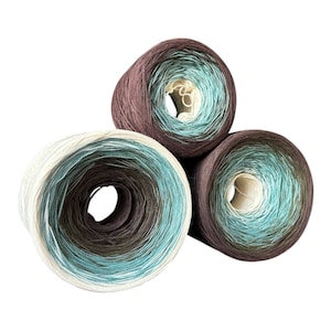 May include: Three yarn cakes in a gradient of colors, including white, teal, brown, and olive green. The yarn is wound in a circular pattern, with a hole in the center of each cake. The yarn is soft and fluffy, perfect for knitting or crocheting projects.