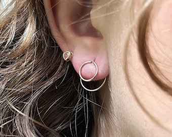 May include: A close-up of a person's ear with two small gold hoop earrings. The earrings are simple and delicate, and they are a popular choice for everyday wear.