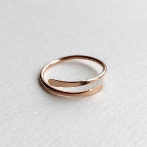 May include: A simple, minimalist rose gold ring with a unique design. The ring is made of a single piece of wire that is bent into a circle and then twisted to create a unique shape.