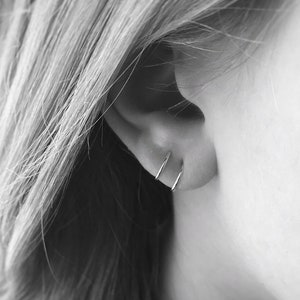 May include: A close-up of a person's ear with two small, silver hoop earrings. The earrings are simple and understated, and they are a great way to add a touch of elegance to any outfit.