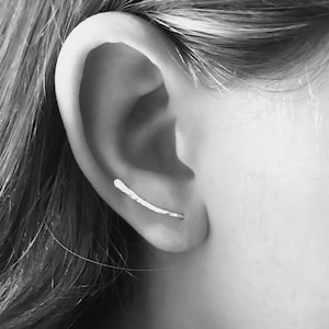 Puede incluir: Un pendiente de aro de plata con un dise&ntilde;o simple y recto. El pendiente se lleva en la parte superior de la oreja, justo por encima del l&oacute;bulo.