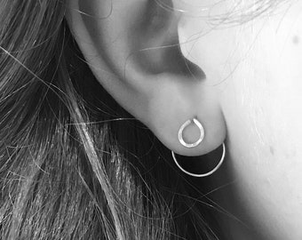 May include: A close-up of a person's ear with two silver earrings. The earrings are a small hoop and a teardrop shape.