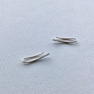 Puede incluir: Dos pendientes de aro de plata, cada uno con un dise&ntilde;o curvo simple. Los pendientes son de metal fino y est&aacute;n dise&ntilde;ados para usarse en la parte superior de la oreja.