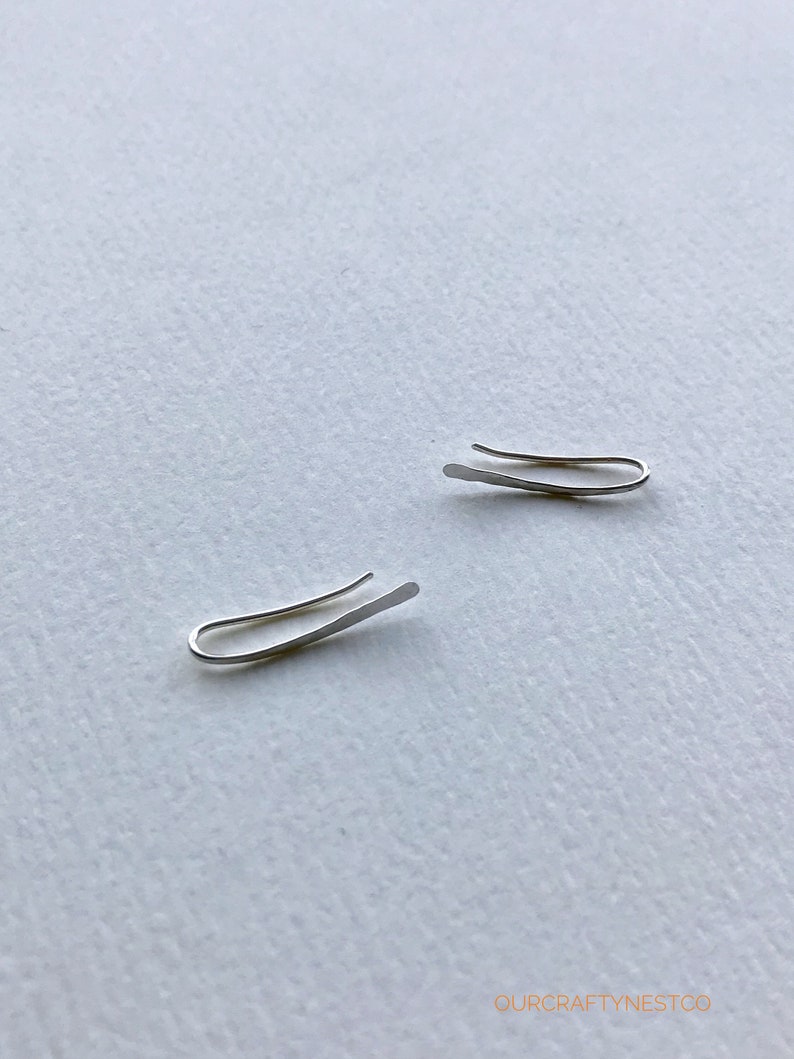 Puede incluir: Dos pendientes de aro de plata, cada uno con un dise&ntilde;o curvo simple. Los pendientes son de metal fino y est&aacute;n dise&ntilde;ados para usarse en la parte superior de la oreja.