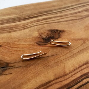 Puede incluir: Un par de pendientes de plata en forma de aro sobre una superficie de madera. Los pendientes son simples y minimalistas.