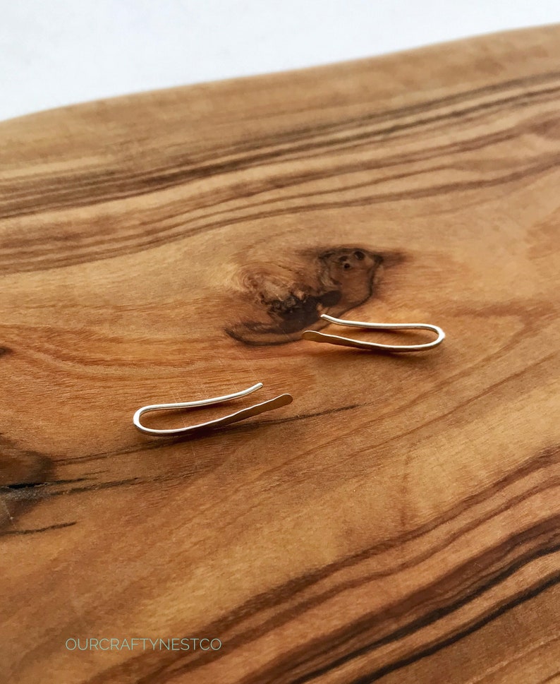 Puede incluir: Un par de pendientes de plata en forma de aro sobre una superficie de madera. Los pendientes son simples y minimalistas.