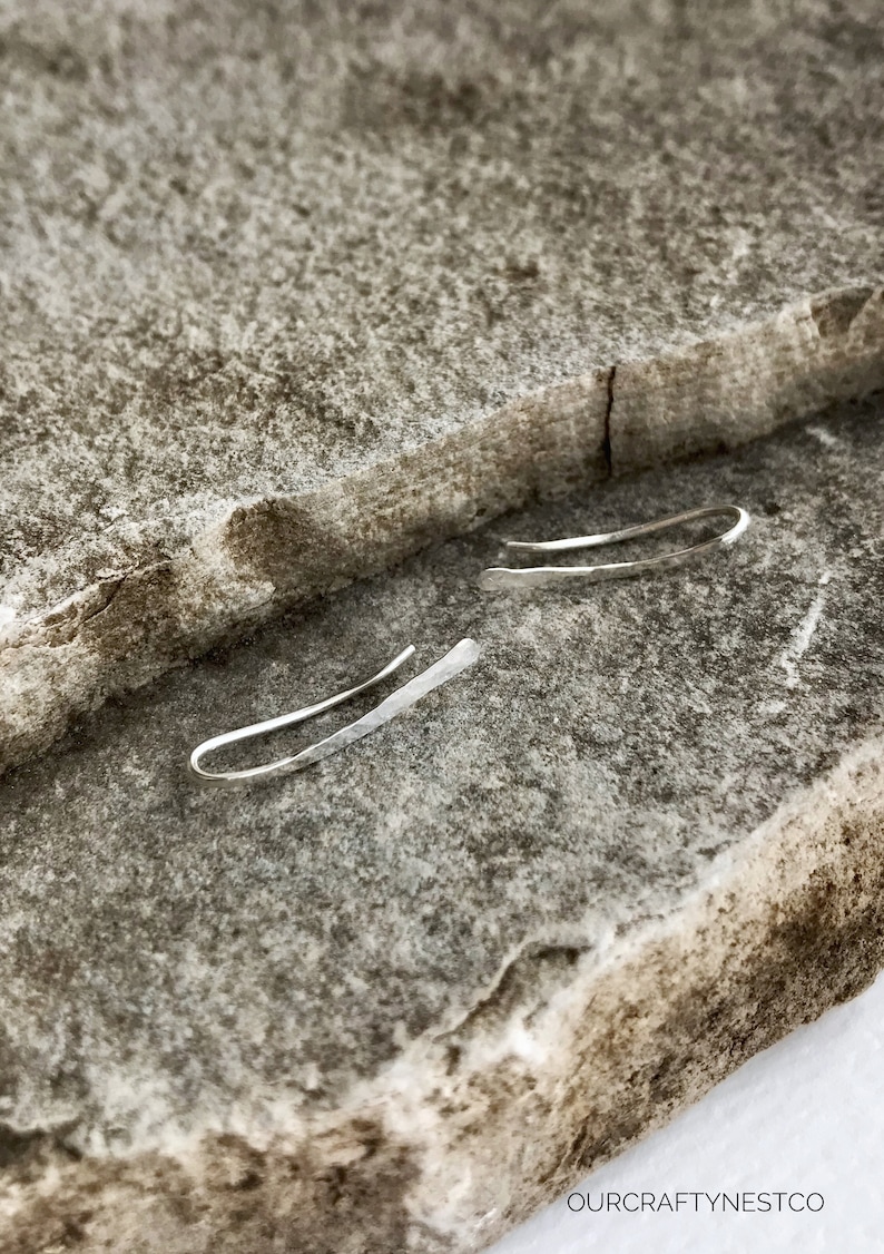 Puede incluir: Un par de pendientes de plata con un dise&ntilde;o simple y curvo. Los pendientes est&aacute;n hechos de metal martillado y tienen un brillo sutil.