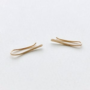 Puede incluir: Un par de clips de oreja de oro, cada uno con una forma curva simple.