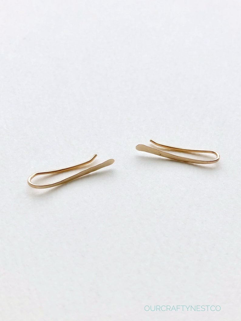 Puede incluir: Un par de clips de oreja de oro, cada uno con una forma curva simple.