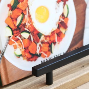 K&ouml;nnte beinhalten: Ein Kochbuchst&auml;nder aus Holz mit einer schwarzen Metallstange. Das Kochbuch ist auf einer Seite mit einem Foto eines Tellers mit Essen und einem Spiegelei ge&ouml;ffnet. Der Buchr&uuml;cken tr&auml;gt die Aufschrift "MULLET".