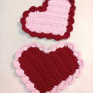 Op de afbeelding: Twee gehaakte harten, één rood met een roze rand en één roze met een rode rand.