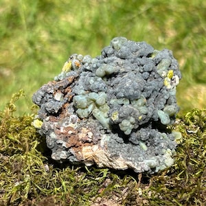 May include: A cluster of green and gray mineral crystals with a rough, textured surface. The crystals are clustered together in a random pattern, creating a unique and interesting display.