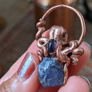 May include: A copper octopus pendant with a purple amethyst stone. The octopus is holding the stone in its tentacles. The pendant is on a copper chain.