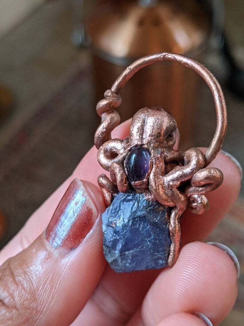 May include: A copper octopus pendant with a purple amethyst stone. The octopus is holding the stone in its tentacles. The pendant is on a copper chain.