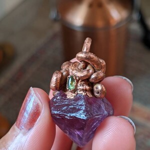 May include: A purple amethyst crystal pendant with a copper wire design and a green gemstone accent.