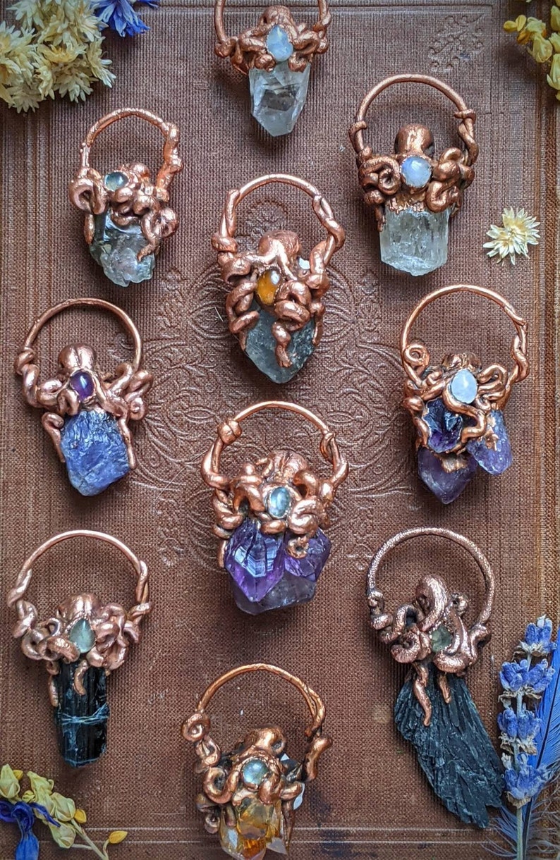 May include: Ten copper wire wrapped crystal pendants with various crystals including amethyst, clear quartz, and black tourmaline. Each pendant features a copper octopus design.
