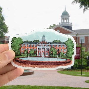 May include: A watercolor illustration of a red brick building with a fountain in front. The building has a white trim and a white cupola. The fountain is surrounded by a brick wall and has a few water jets. The building is surrounded by trees.