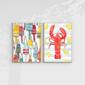 May include: Two framed watercolor prints. One features colorful buoys in yellow, red, blue, and green. The other print shows a red lobster with lemon slices on a blue and white striped background. Both prints have a coastal theme.