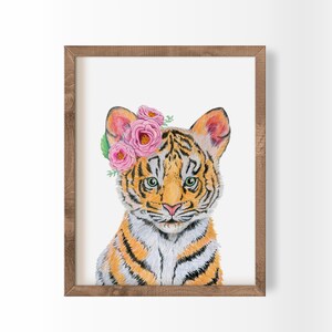 May include: A framed watercolor print of a tiger cub with orange and black stripes, wearing a crown of pink roses and green leaves. The tiger has green eyes and a pink nose. The frame is made of brown wood.
