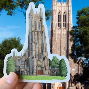 May include: A sticker of a detailed illustration of a tall, gray stone church with a pointed roof and arched windows. The sticker is held in front of a larger version of the same church.