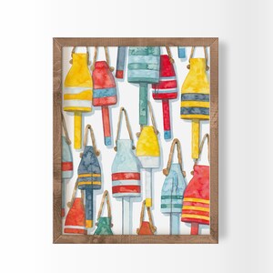 May include: Watercolor print of colorful buoys in yellow, red, blue, and green, with rope handles, set against a white background. The buoys have horizontal stripes and are framed in a wooden frame. Nautical themed art.